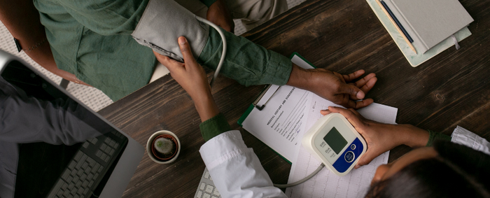 Arzt misst den Blutdruck eines Patienten mit einem elektronischen Blutdruckmessgerät am Schreibtisch