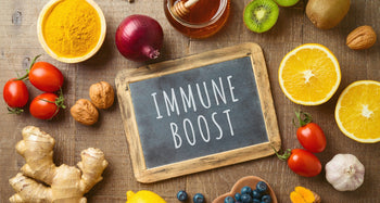 Verschiedene Lebensmittel wie Nüsse, Tomaten, Zwiebeln und Ingwer liegen auf einem Holztisch. In der Mitte liegt eine Tafel mit der Aufschrift 