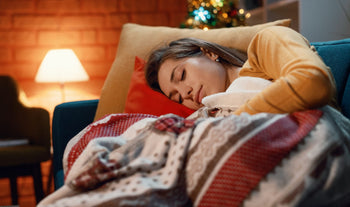 Eine junge Frau liegt mit einer Decke auf dem Sofa und schläft.